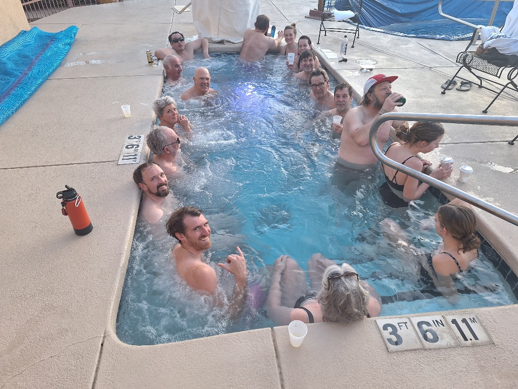 Over a dozen OKC Ski Club members relaxing together in a giant outdoor hot tub at El Pueblo Lodge during the 2025 Taos ski and snowboard trip.